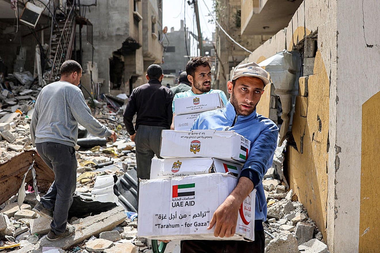 Men walk past damaged buildings with aid packages collected from an air drop over the northern Gaza Strip on April 23, 2024. Photo by AFP via Getty Images.