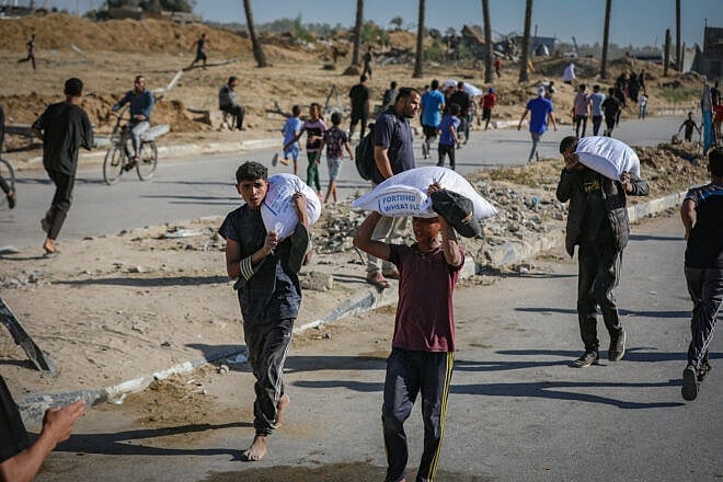 Palestinians carrying sacks of flour outside a Gaza Humanitarian Relief Foundation distribution point in Deir al-Balah, the central Strip, May 28, 2025. Photo by Ali Hassan/Flash90.
