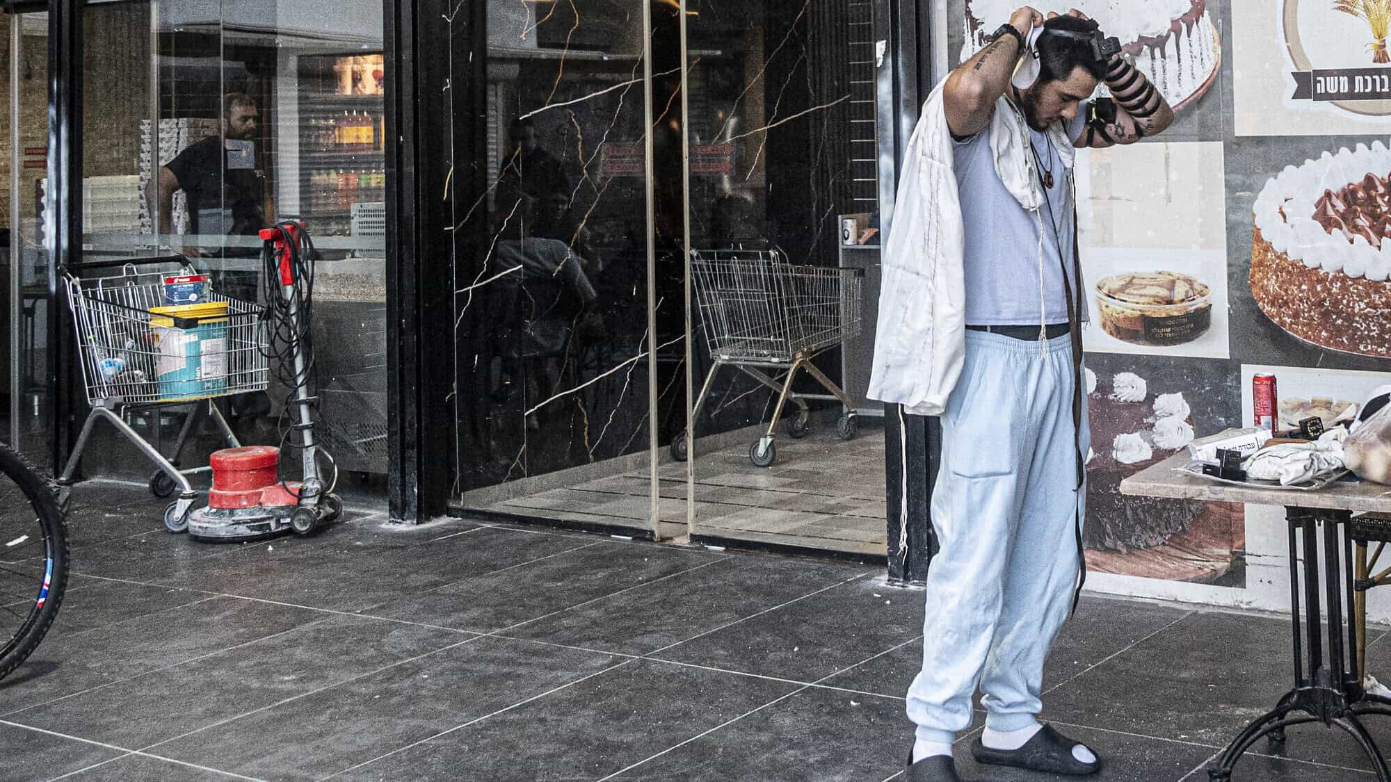Ouriel Hattab puts on tefillin outside a bakery in Kiryat Yam, Israel, on June 15, 2025. Photo by Canaan Lidor.