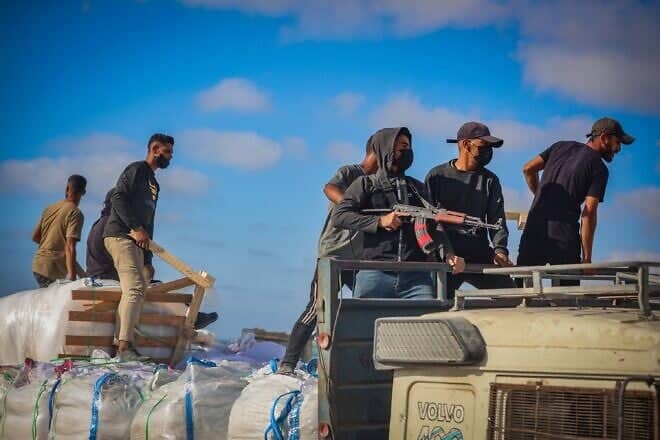 Armed Palestinians sit on trucks carrying humanitarian aid near the Zikim border crossing between Israel and Beit Lahia in the northern Gaza Strip, June 25, 2025. Photo by Ali Qariqa/Flash90.