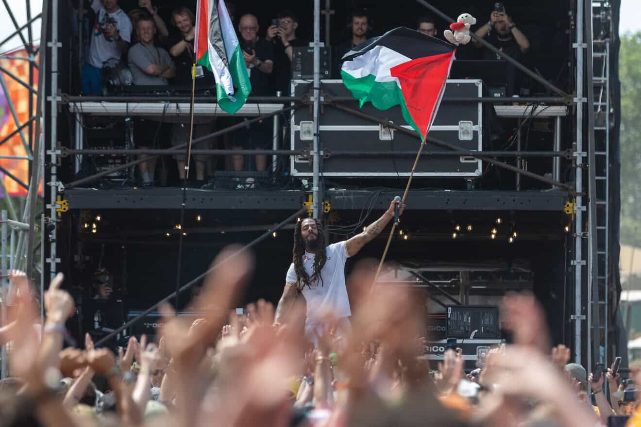 Bob Vylan waves a Palestinian flag as he performs on the West Holts stage on day four of Glastonbury Festival 2025 at Worthy Farm, Pilton in Glastonbury, England, on June 28, 2025. Avon and Somerset Police have announced a criminal investigation into the performances of Bob Vylan and the Irish-language rap band Kneecap, known for making pro-Palestinian comments during their live performances. Photo by Matt Cardy/Getty Images.