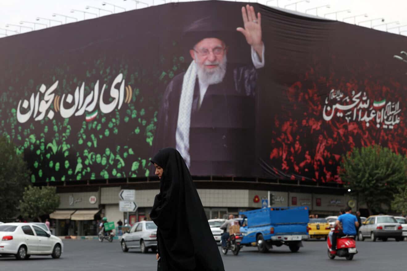 An Iranian crosses a street next to a billboard bearing the portrait of Iranian Supreme Leader Ayatollah Ali Khamenei at Enqelab Square in Tehran, July, 9, 2025. Photo by AFP via Getty Images.