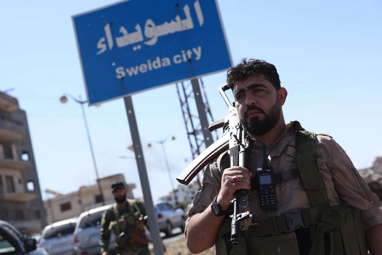 A member of Syria's security forces stands under a sign in the predominantly Druze city of Sweida, following clashes between Bedouin tribes and Druze fighters on July 15, 2025. Photo by Bakr Alkasem/AFP via Getty Images.