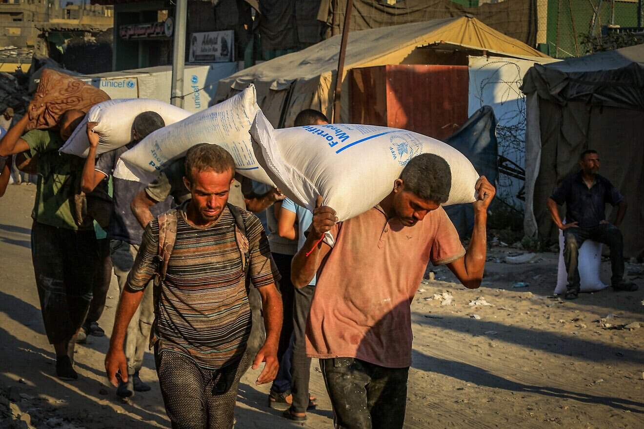 Palestinians carry bags of flour after humanitarian aid trucks arrived via the Israeli-controlled Kerem Shalom border crossing into Khan Yunis, in southern the Gaza Strip, July 24, 2025. Photo by Abed Rahim Khatib/Flash90.