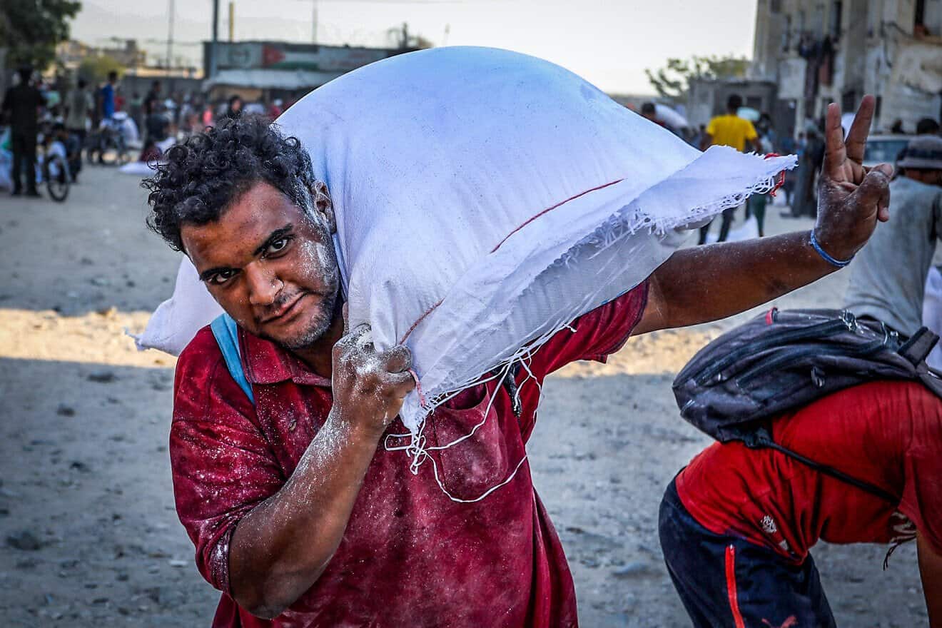 A Palestinian Arab man carries a bag of flour after trucks with humanitarian aid arrived via the Israeli-controlled Kerem Shalom crossing into in Khan Yunis, in southern Gaza, on July 24, 2025.  Photo by Abed Rahim Khatib/Flash90.