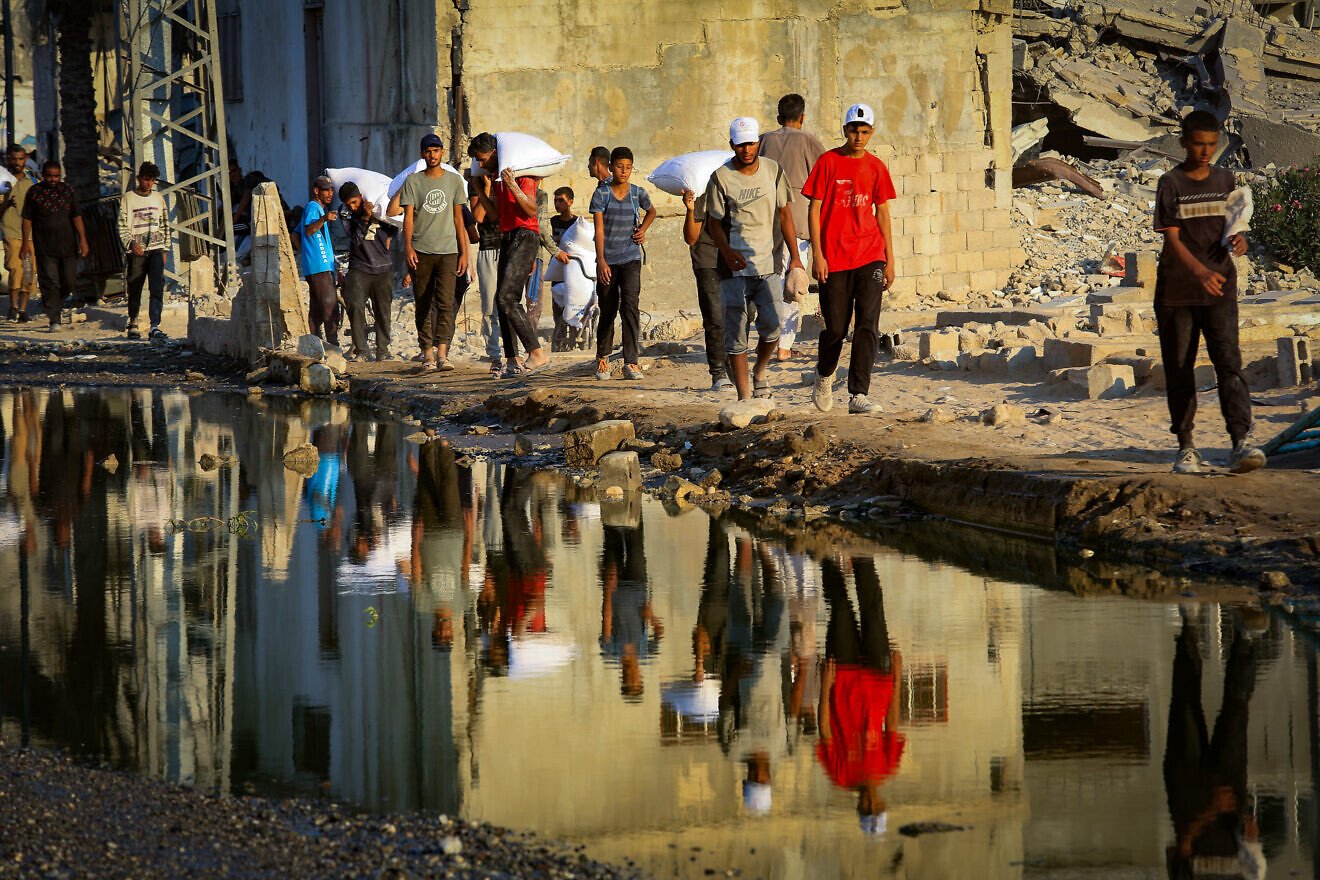 Palestinians carry bags of flour after humanitarian aid trucks arrived via the Israeli-controlled Kerem Shalom border crossing into Khan Yunis in southern the Gaza Strip, July 24, 2025. Photo by Abed Rahim Khatib/Flash90.