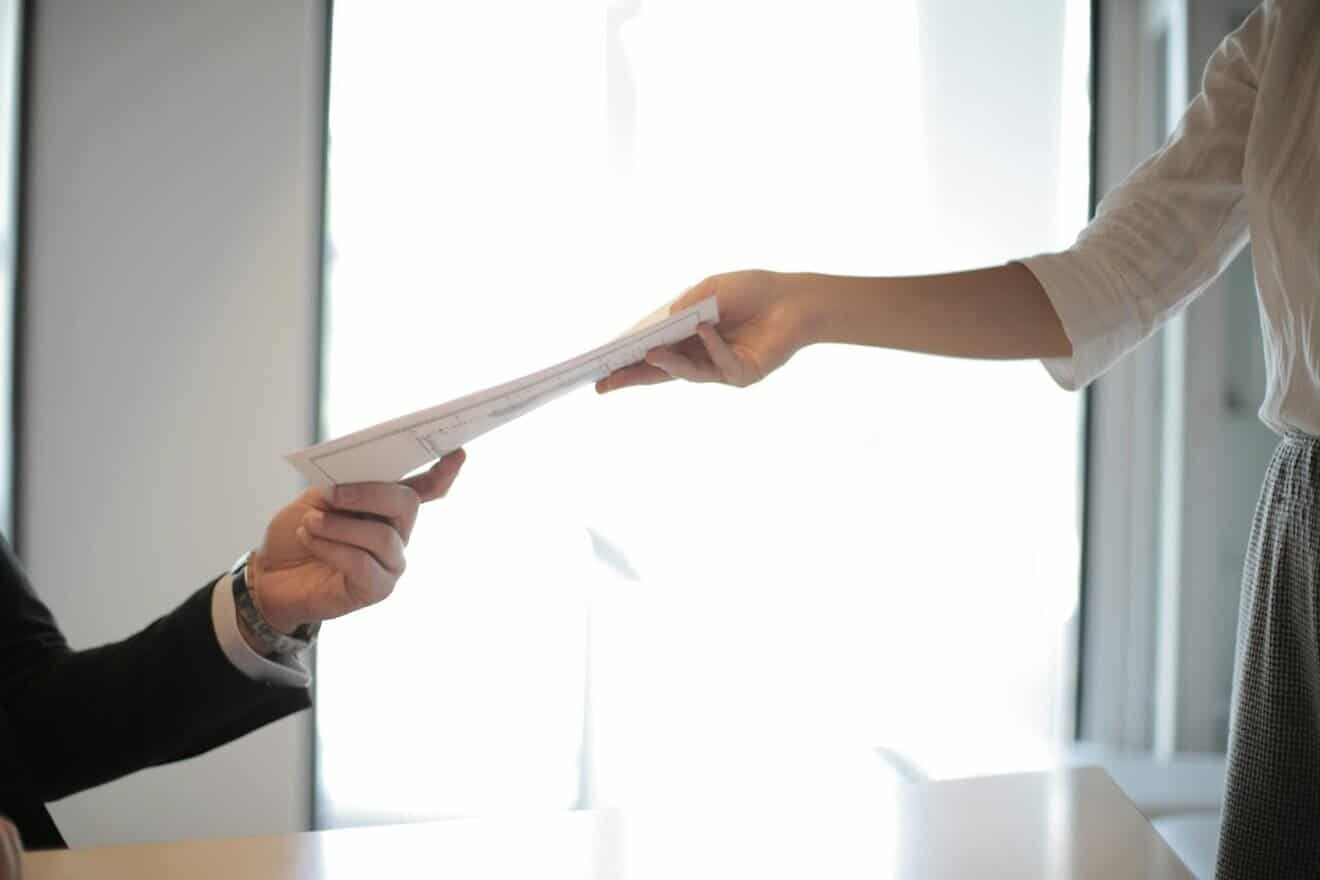Employee handing paperwork across a desk. Credit: Andrea Piacquadio/Pexels.