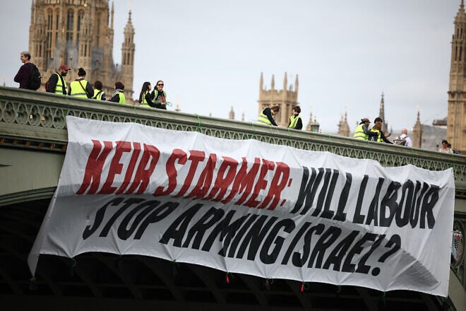 A banner reading “Keir Starmer: Will Labour Stop Arming Israel?” is hung over the side of Westminster Bridge in front of the Palace of Westminster, home to the Houses of Parliament, during early morning rush hour in London on June 3, 2024. Photo by Photo by Henry Nicholls/AFP via Getty Images.