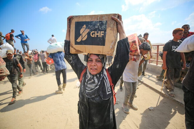 Palestinians carry food and supplies from a Gaza Humanitarian Foundation aid distribution point at the Netzarim corridor in central Gaza, Aug. 1, 2025. Credit: Ali Hassan/Flash90.